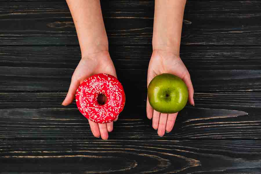 Mãos segurando um donut e uma maça.