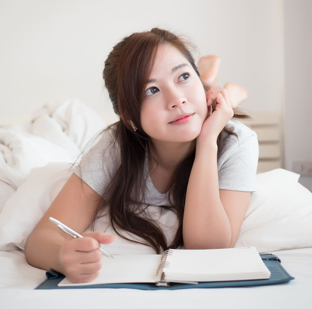 Pretty woman happy and relax to write reflective diary on her bed.