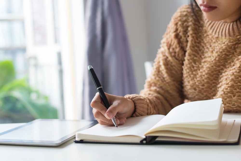 Close-up of pensive woman writing out ideas in journal.